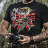 Mand iført M-Tac T-Shirt Kamikaze Spirit med FPV-design, holder en dronecontroller. Sort t-shirt med stiliseret kranieprint.