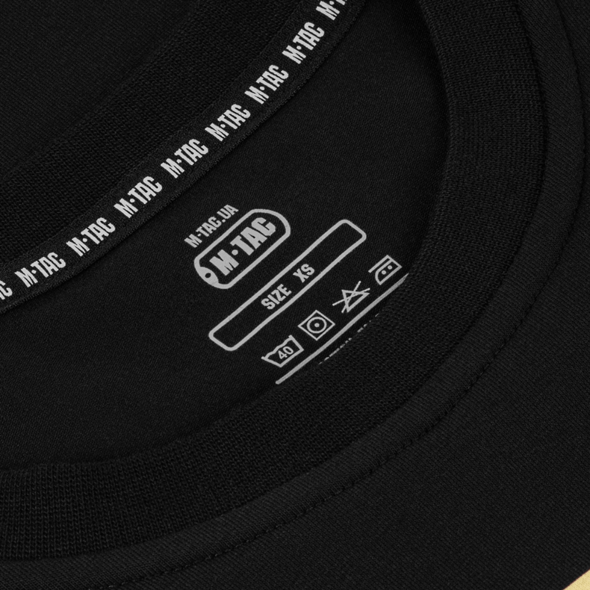 Nærbillede af M-Tac T-Shirt Logo med fokus på mærketiketten og størrelsen XS, der fremhæver det ikoniske design og kvalitet.