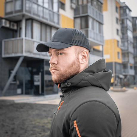 Mand iført en sort M-Tac Mesh Flex Ripstop Baseball Cap foran bybygninger, viser udendørs holdbarhed og stil.