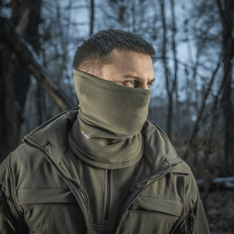 Mand bærer M-Tac Tube Scarf Polartec i skoven som ansigtsmaske, beskytter mod kulde og vind under udendørsaktiviteter.