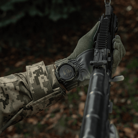 M-Tac Tactical Ur med Kompas 2233 båret af person i camouflage med riffel, viser holdbarhed og funktionalitet i vildmarken.