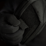 Person iført sort handske justerer M-Tac Patch Valknut Laser Cut Odin symbol på en jakke. Taktisk udstyr med velcro.