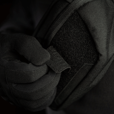 Person iført sort handske justerer M-Tac Patch Valknut Laser Cut Odin symbol på en jakke. Taktisk udstyr med velcro.