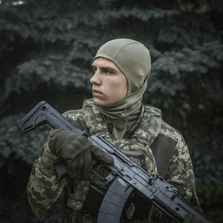 Soldat iført M-Tac Sweater-Ninja-Balaclava Premium i skovklædning, holder våben, optimal til fugthåndtering og komfort.