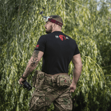 Mand bærer M-Tac T-Shirt Kamikaze Spirit med FPV-goggles og tatovering, stående i naturen.