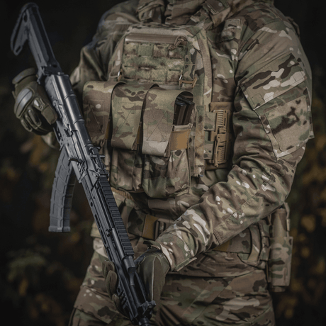 Person i camouflageuniform med M-Tac taske til 2 magasiner i brug og gevær i hænderne, illustrerer taktisk militærudstyr.