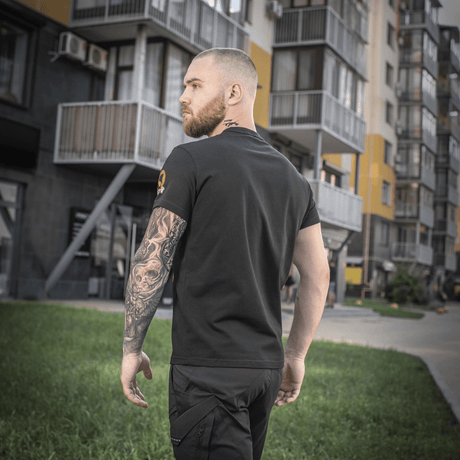 Mand bærer en M-Tac T-shirt Black Sea Expedition foran moderne bygninger